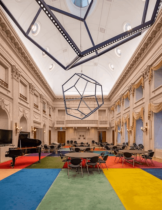 Oude Zaal met veelkleurig tapijt en uit vijfhoeken opgebouwde kroonluchters