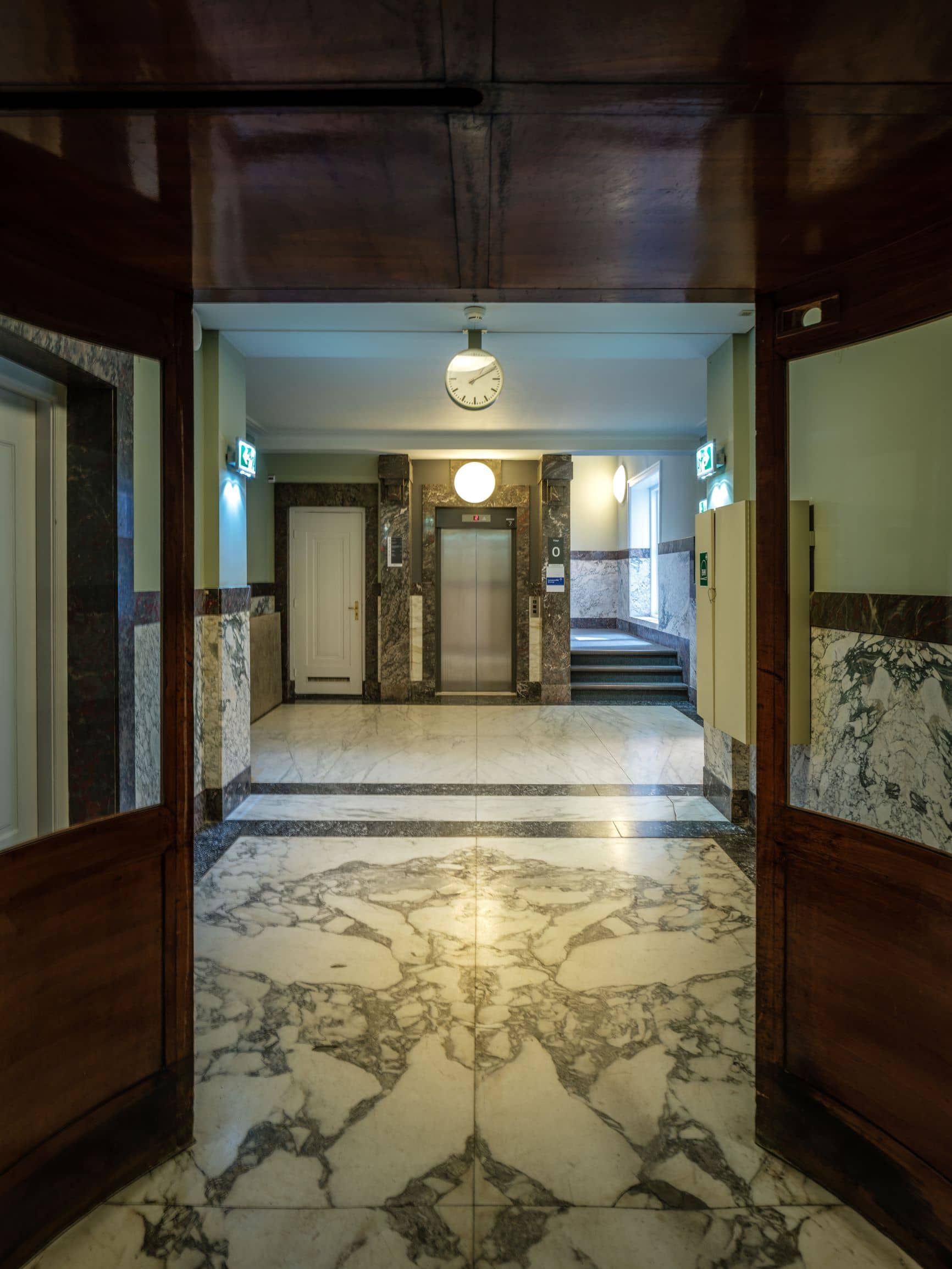 Entreehal met natuurstenen vloer en lift en trap op de achtergrond