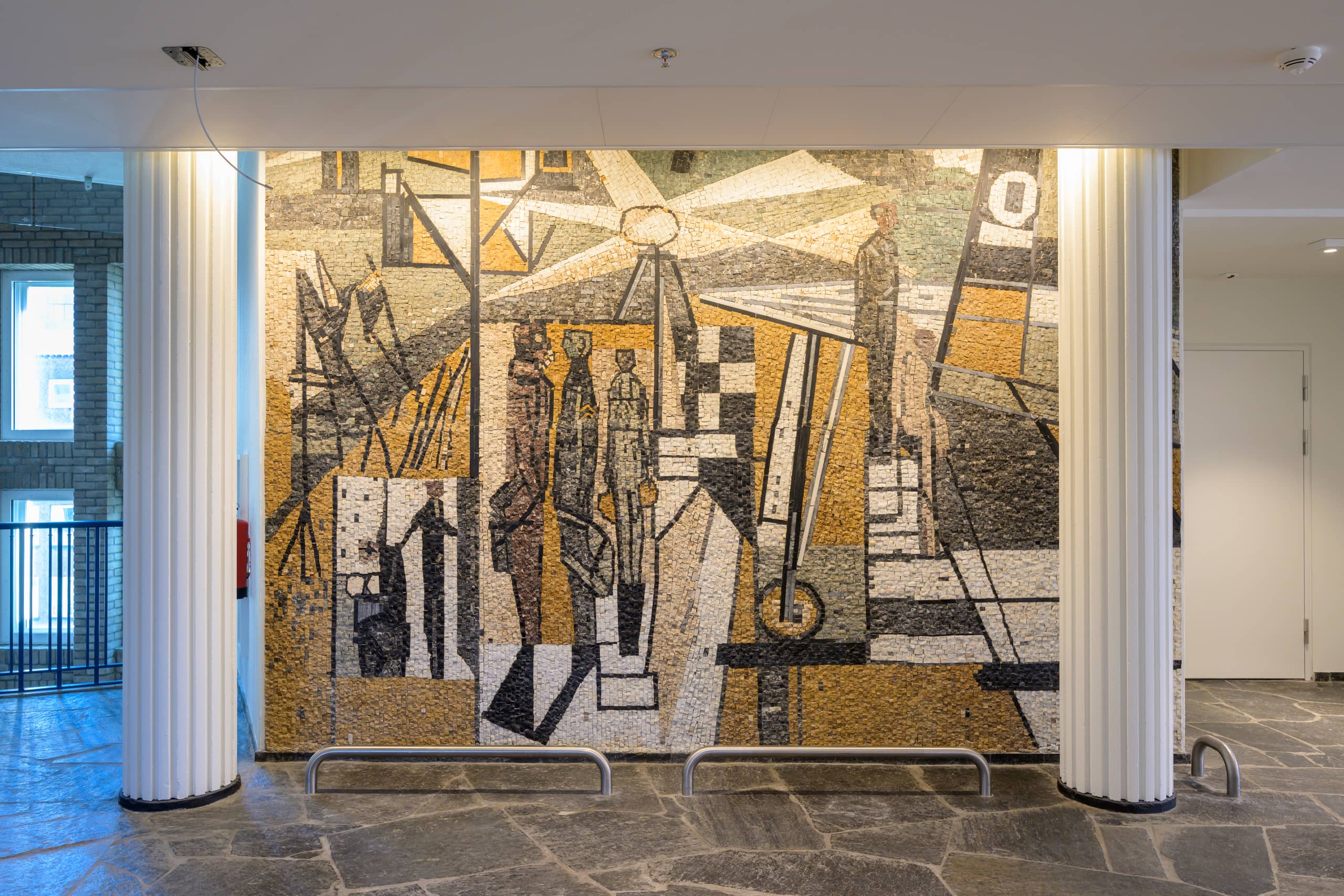 Mozaïek met gestileerde figuren op kleurige ondergrond in tijdelijke huisvesting ministerie AZ