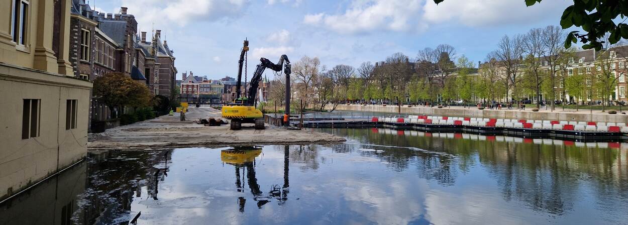 Aanleg van het werkgebied Hofvijver; een installatie is bezig damwanden te plaatsen langs een met zand gedempt gedeelte van de vijver