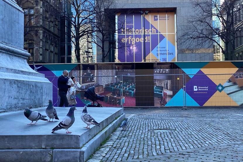 Duiven en passanten op het Plein in Den Haag met op de achtergrond de versierde bouwhekken van de Binnenhofrenovatie