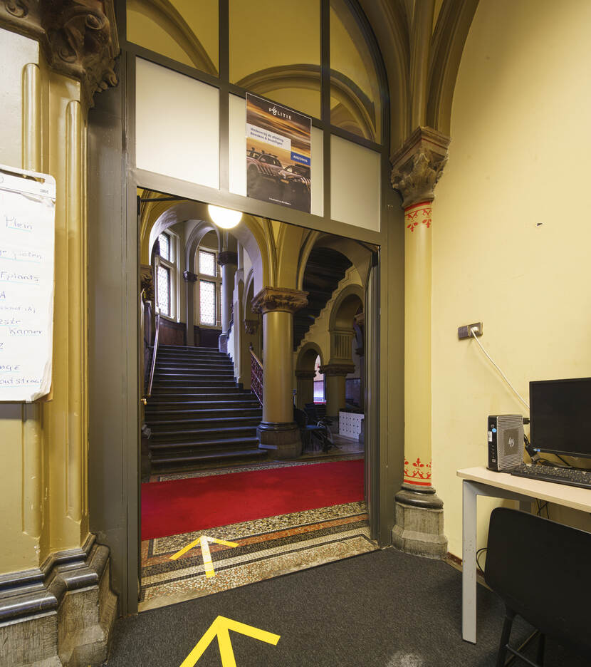 Vestibule gebouw J voor renovatie met werktafel en de doorgang naar het trappenhuis