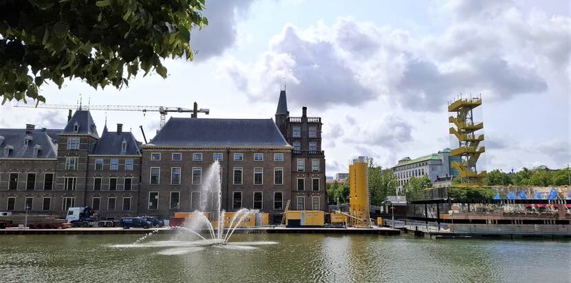 De Hofvijver met fontein en op het werkgebied tegen de gevel van de Eerste Kamer twee gele silo's en een aantal gele containers