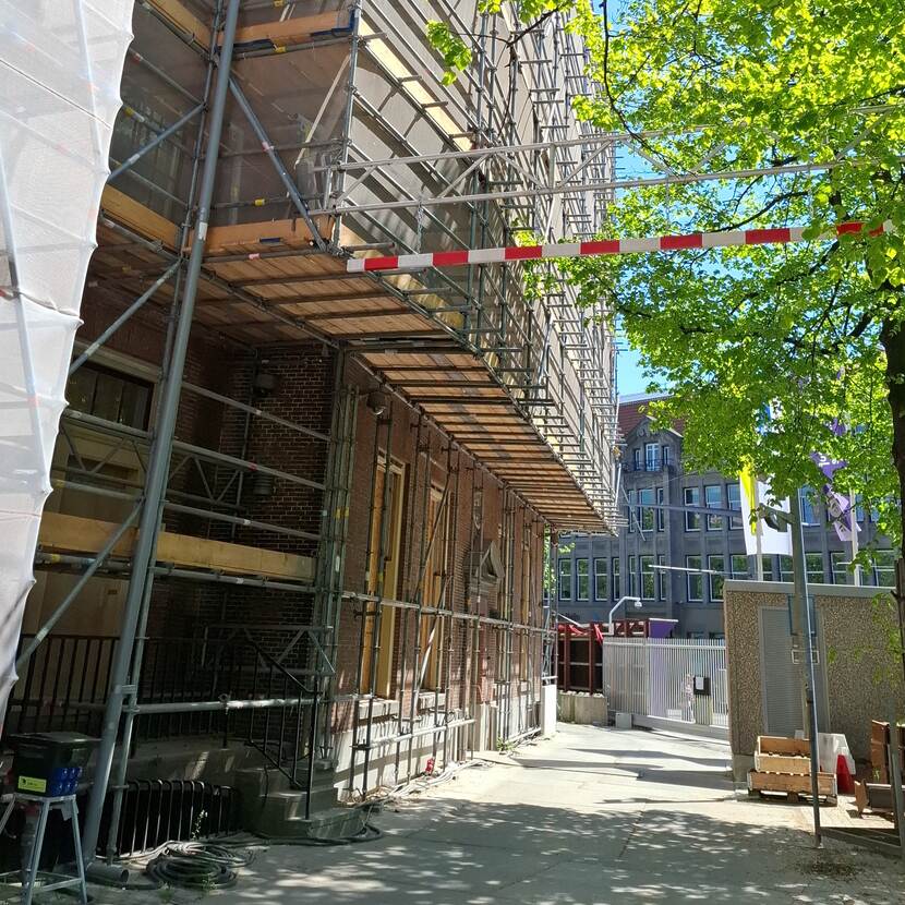 Met 'zwevende' steiger ingepakte gevel van gebouw A van de Tweede Kamer aan het Buitenhof; een roodwitte lat geeft de hoogte aan voor het verkeer