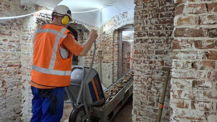 Werknemer leegt kruiwagen met bouwafval op een lopende band