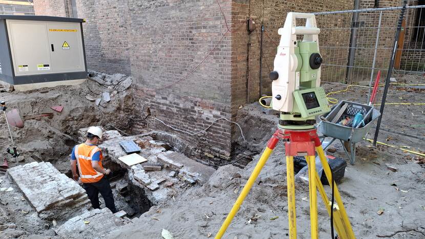 Archeoloog bij funderingsresten achter de Grafelijke Zalen, op de voorgrond een geosysteem op statief