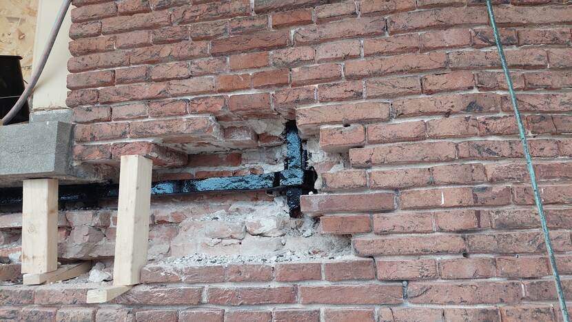 Achter een gat in de bakstenen muur is een zwart muuranker zichtbaar