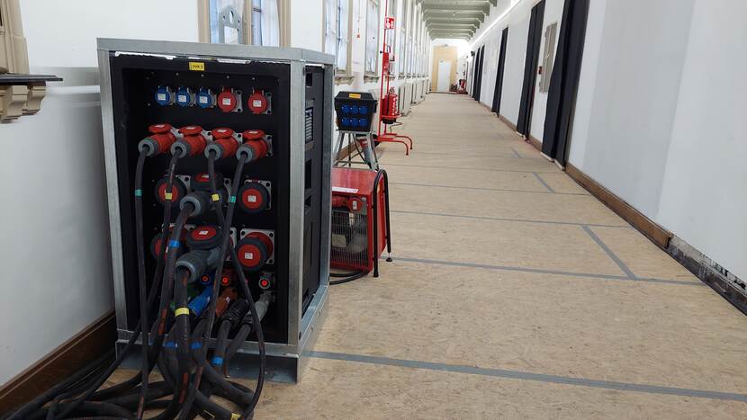 In de lange gang van de Raad van State staat een grote stekkerbox van 50 x 50 cm en 1 meter hoogte waarop verschillende kabels zijn aangesloten
