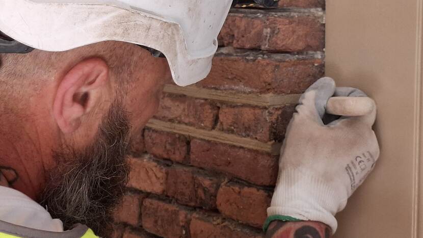 Bouwmedewerker werkt een voeg bij naast een kozijn bij gebouw A van de Tweede Kamer