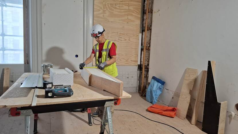 Timmerman op werktafel bezig met het opmeten van een vervangend stuk kozijn voor de gevel aan het Buitenhof