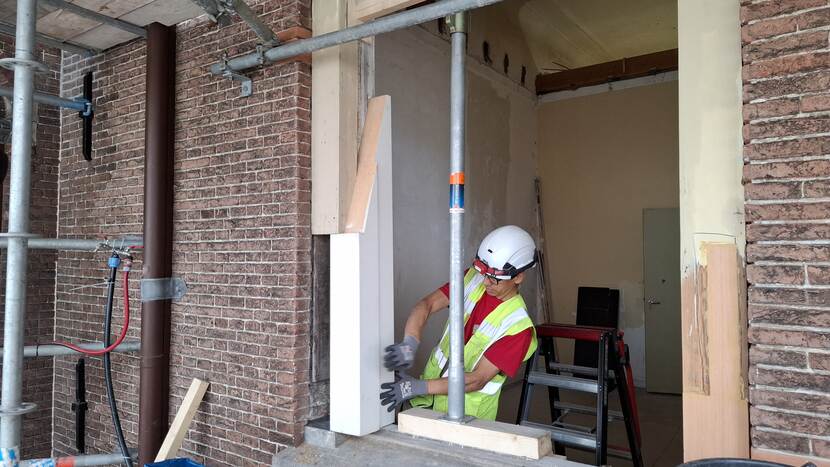 Timmerman bezig met het plaatsen van een vervangend deel van een kozijn in gebouw A van de Tweede Kamer