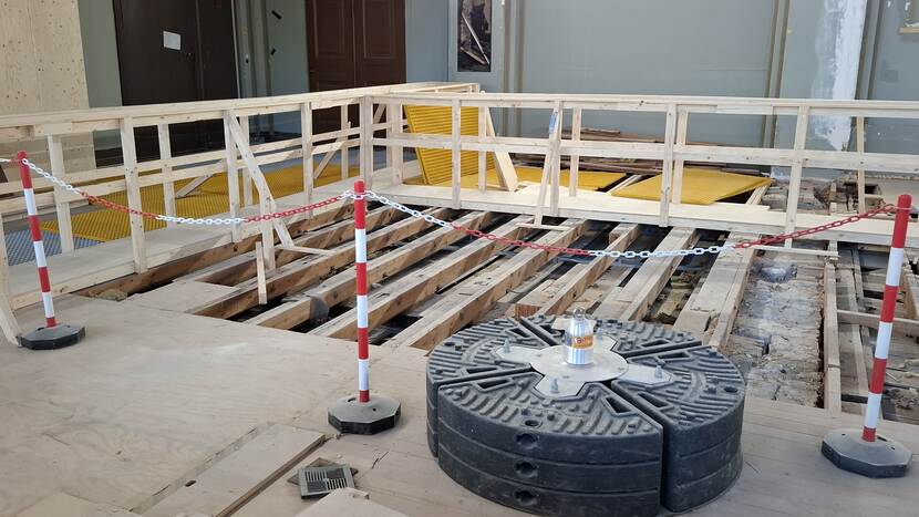 Blootgelegde balken in de plenaire zaal van de Eerste Kamer, over de balken ligt een loopbrug, op de voorgrond is een contragewicht te zien