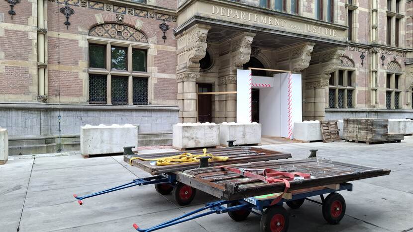 Twee zware deuren op twee karretjes bij de oude ingang van gebouw J aan het Plein, boven de ingang het opschrift 'Departement van Justitie'
