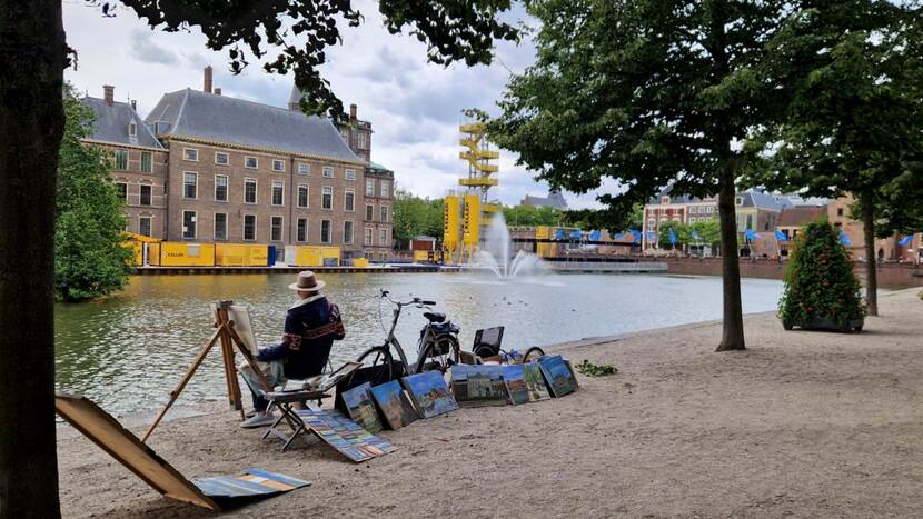 Landsschapsschilder kijkt vanaf Lange Vijverberg naar het werkgebied, hij heeft een aantal schilderijen bij zijn schildersezel uitgestald