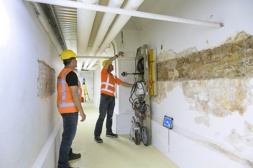 Twee onderzoekers voeren in een keldergang een scanapparaat langs de kelderwand van de voormalige Hofkapel