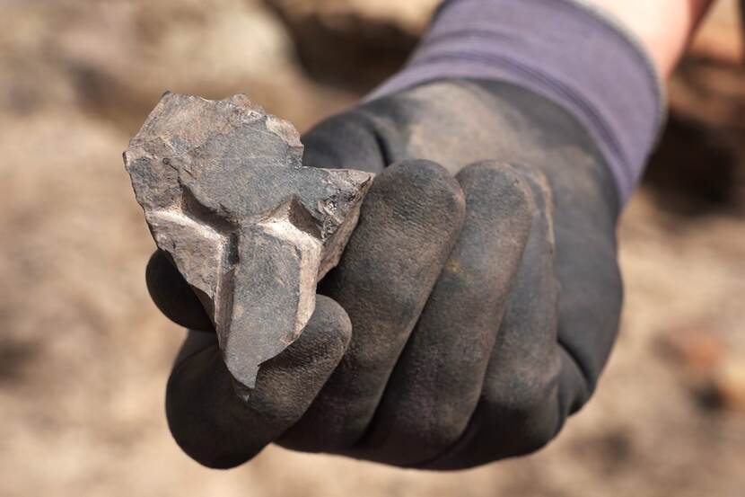 Een archeoloog houdt een klein stukje van een grafzerk tussen de vingers