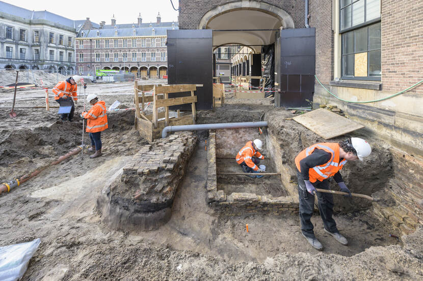 Vier archeologen van de gemeente Den Haag aan het werk onder het in 1879 gesloopte deel van de Hofkapel met rechts zichtbaar de gevonden grafkelder