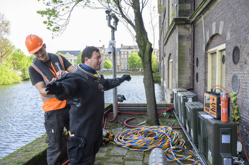 Een duiker wordt door een medewerker in het duikpak geholpen