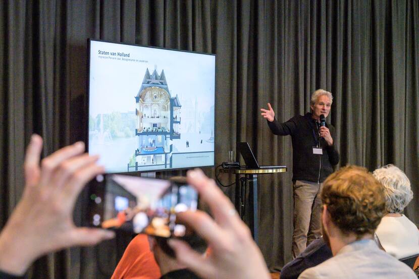 Architect Joep Mol bij zijn presentatie van het ontwerp voor de Eerste Kamer, op het beeldscherm is een doorsnede over de plenaire zaal te zien