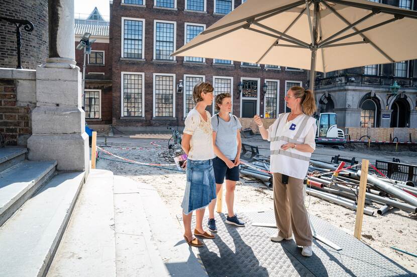 Een medewerker geeft onder een parasol uitleg aan bezoekers op het Opperhof op Open Monumentendag Binnenhof 2023