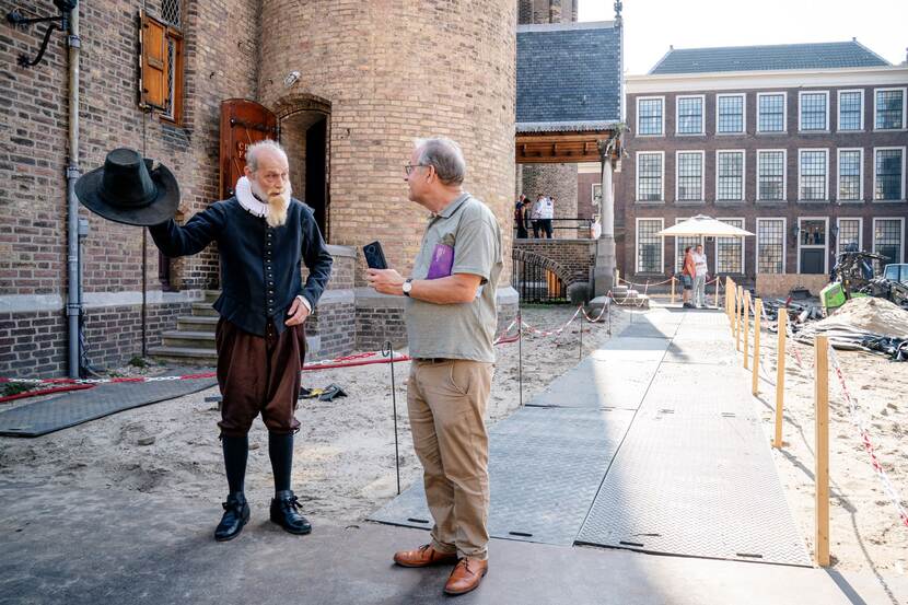 Een als Johan van Oldenbarnevelt verklede acteur geeft een bezoeker vlak voor de Ridderzaal uitleg op Open Monumentendag Binnenhof 2023