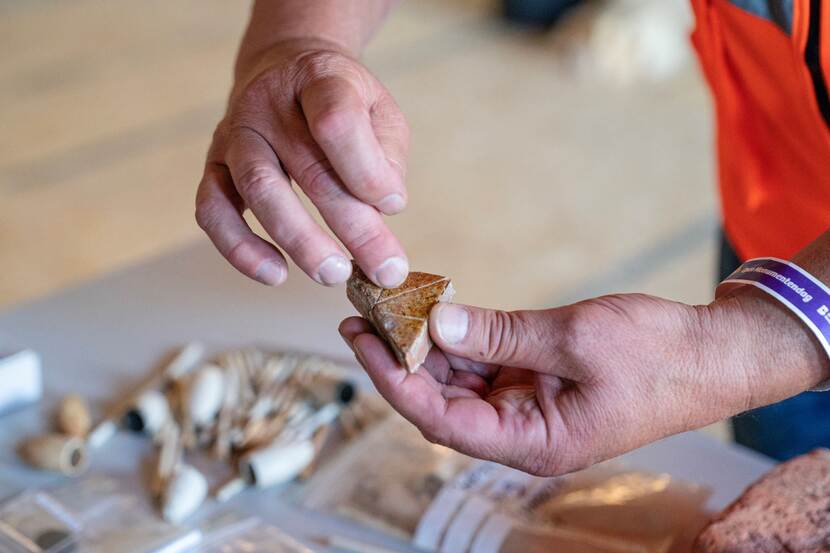 Een archeoloog houdt een klein stukje van een gevonden tegel tussen de vingers op Open Monumentendag Binnenhof 2023