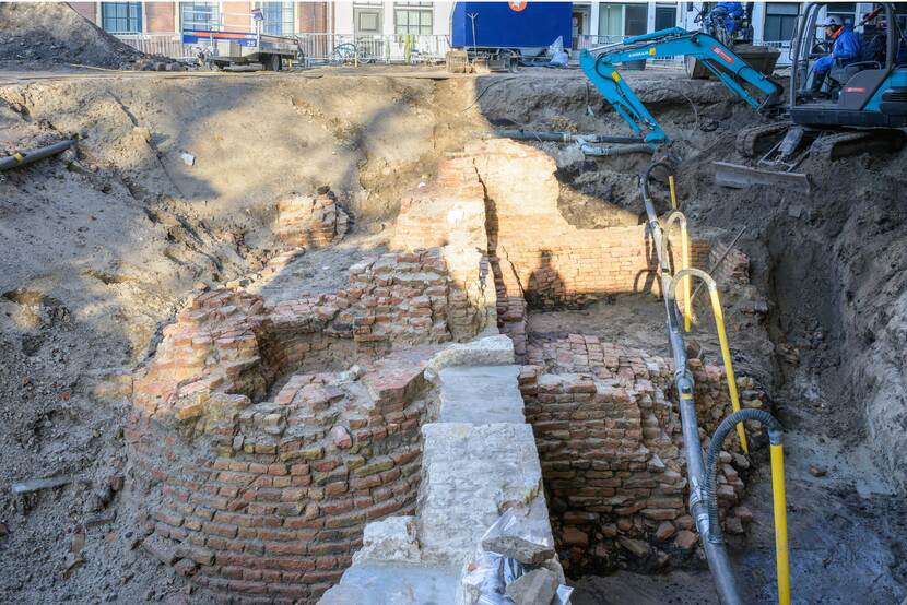 Het blootgelegde fundament van een van de torens en muren van de Spuipoort. Op de achtergrond rechts is een elektrische graafmachine aan het werk.