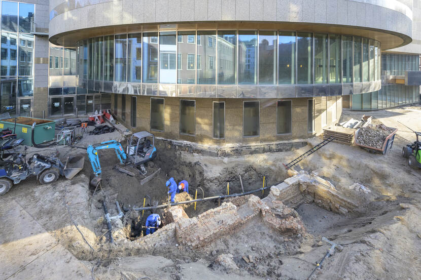 Archeologen aan het werk bij de blootgelegde ondergrondse resten van de Spuipoort. Op de achtergrond de pleniare zaal van de Tweede Kamer.