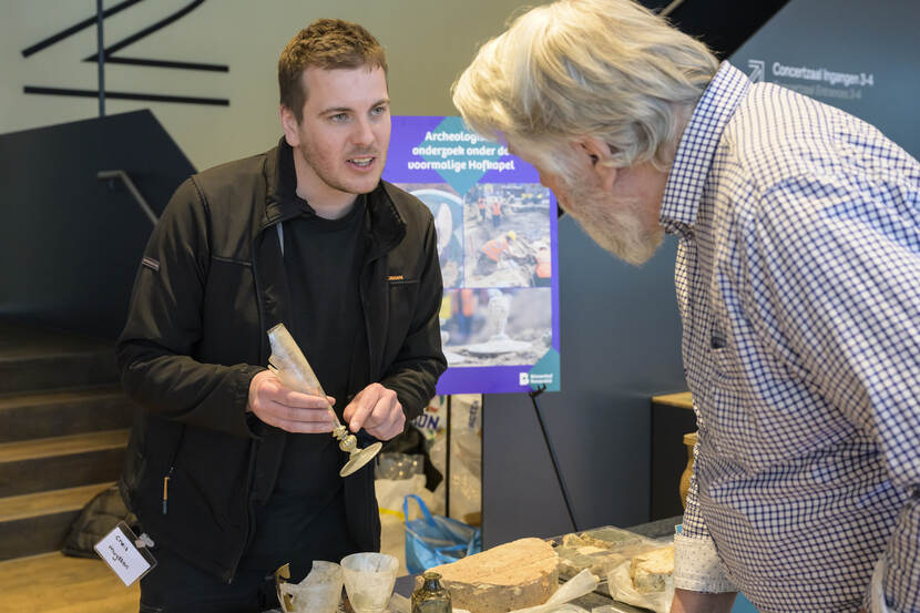 Bezoeker kijkt belangstellend naar glaswerk bij de informatiekraam archeologie