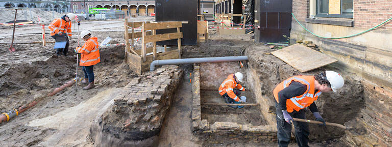 Vier archeologen aan het werk bij de voormalige Hofkapel. In het midden is de kleine grafkelder zichtbaar.